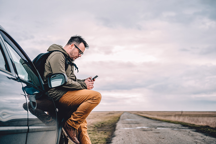 Man using phone while leaning on car by the side of road